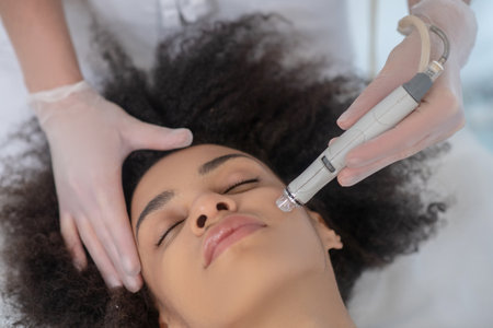 Facial treatment. Close-up of young woman face with closed eyes during cosmetology hardware...