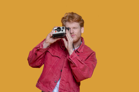 Old camera. Red-haired bearded young man with old camera making photosの写真素材