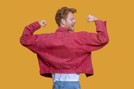 Showing muscles. Red-haired bearded young man in red jacket showing musclesの写真素材