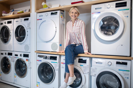 Showroom. Blonde woman in striped shirt sitting on a washing machineの写真素材
