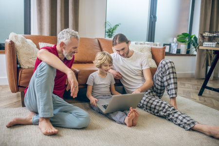 Watchin video. Two men and their son watching something on a laptopの写真素材