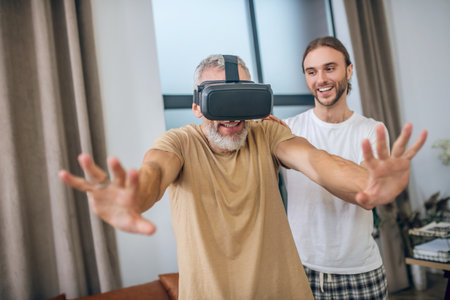 VR glasses. Man in vr glasses walking in the room, his partner supporting him