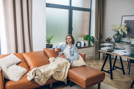 At home. Long-haired man in jeans shirt spending time at home