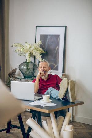 Bored from work. Grey-haired man sitting at the laptop and looking bored