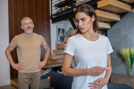Unexpected pregnancy. Young dark-haired woman looking stressed while looking at the pregnancy test...