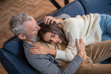 Tenderness. Grey-haired man sitting on the sofa and hugging his wife with tendernesの写真素材