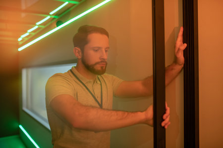 Glass transparent door. Serious young adult man leaving room opening transparent glass door at work