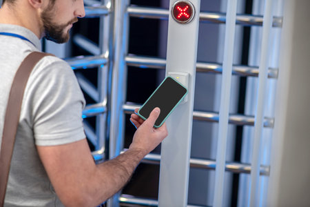 Ingress protection. Bearded young man applying smartphone to access scanner at turnstile of entrance...