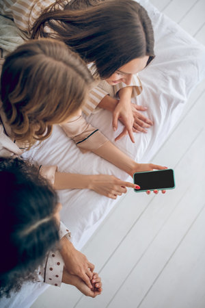 Social network. Girls lying on bed and watching something on a smartphoneの写真素材