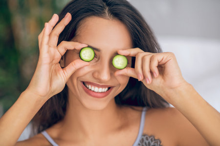 Organic cosmetics. Brunette girl with slices of cucumber in handsの写真素材