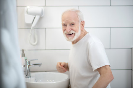Senior man. Smiling gray-haired man in white tshirt in the bathroomの写真素材