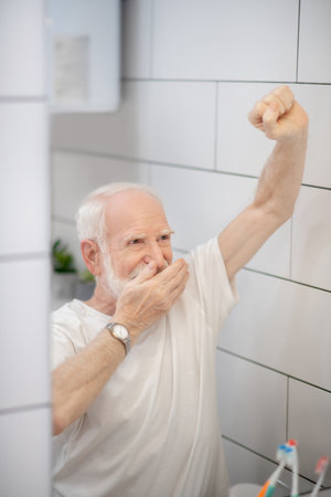 Feeling sleepy. Gray-haired man in white tshirt feeling sleepy and stretchingの写真素材