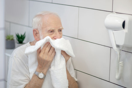 After shaving. Gray-haired man in white tshirt wiping his face with the towelの写真素材