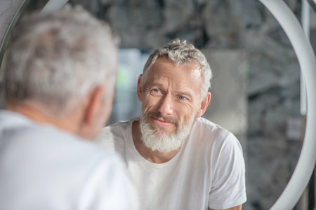 Checking an appearance. A grey-haired man looking at his reflection in the mirror