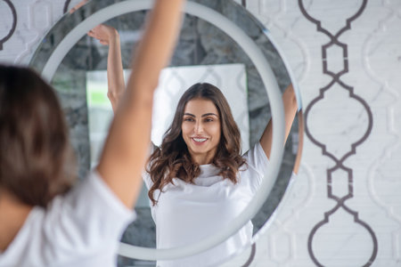 Morning routine. A woman stretching her hands near the mirrorの写真素材