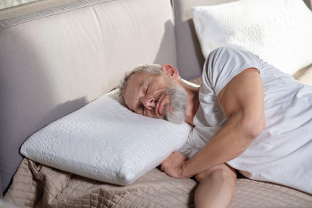 Daytime sleep. Adult bearded man in white ball cap lying with closed eyes on bedの写真素材