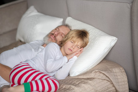 Restful sleep. Peaceful child with dad lying on white pillows on bed sleeping at home during day