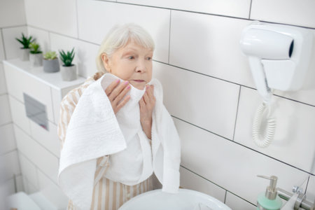 Washing up. Gray-haired woman drying her face with the towelの写真素材