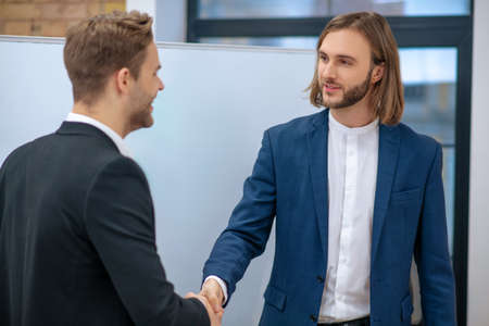 Success, agreement. Two young adult successful men in dark suits and white shirts shaking hands...