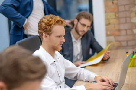 Professionalism. Redhaired serious concentrated man working at laptop and colleagues managers busy...