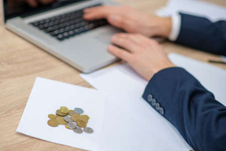 Few coins. Few money coins lying on the table near male hands and laptop