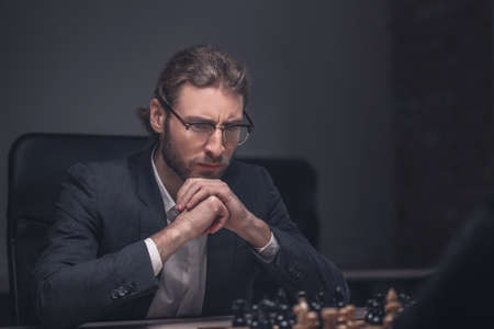 Hobby, interest. Serious involved young man in glasses sitting with his hands on his chin in front...