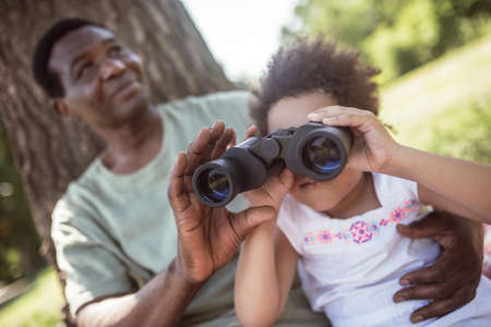 Binocular. Dark-skinned man showing a binocular to his daughter