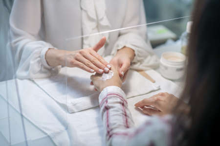 Hands moisturizing. Close up picture of beautician hands applying cream on clients handsの写真素材