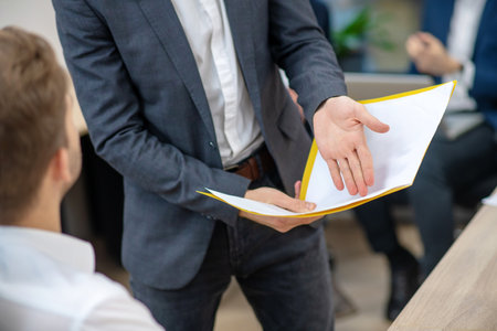 Search for truth. Male hands holding yellow folder pointing at document indoors face not visibleの写真素材