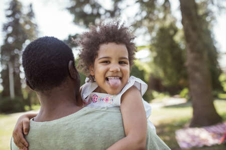 Having fun. Cute curly kid sitting playing with her dad and showing tongueの写真素材