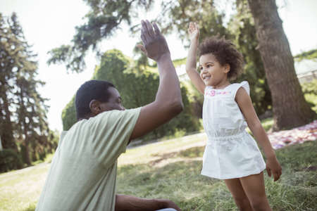 High five. Cute curly kid sitting playing with her dad and doing high fiveの写真素材