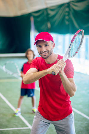 Tennis player. Young bearded man in a red cap waving a tennis racketの写真素材