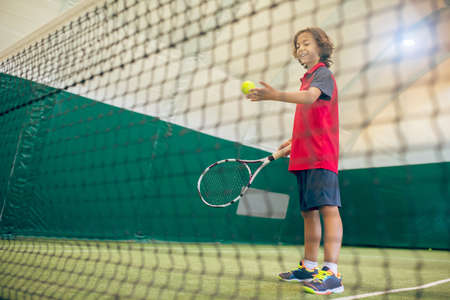 Tennis. Dark-haired boy in red tshirt ready to hit the tennis ballの写真素材