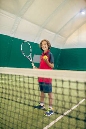 Tennis. Dark-haired boy in red tshirt ready to hit the tennis ballの写真素材