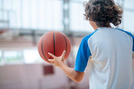 Basketball. Dark-haired boy in sportswear playng basketball in a gym