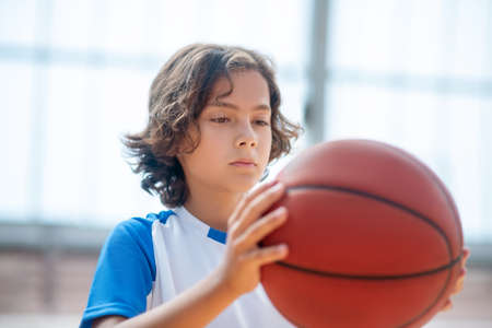 Playing basketball. Dark-haired boy in sportswear holding a ball and looking seriousの写真素材