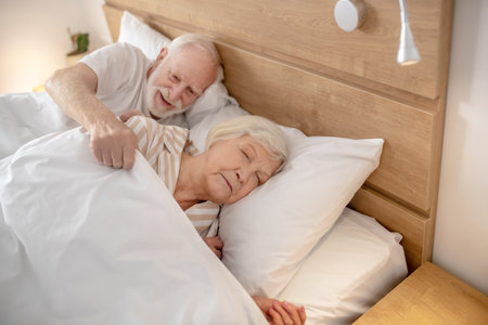 Ready to sleep. Elderly man covering his wife with the blanketの写真素材