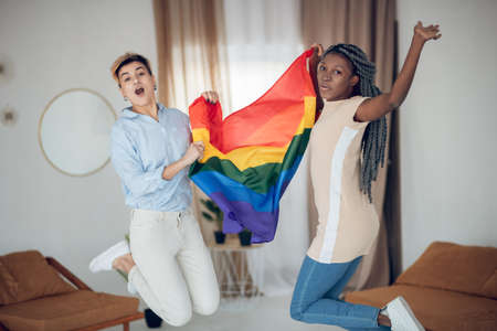Joyful mood. Two young girls holding a rainbow flag and jumpingの写真素材