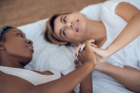 Closeness. Two girls lying on the bed, holding hands and looking at each other