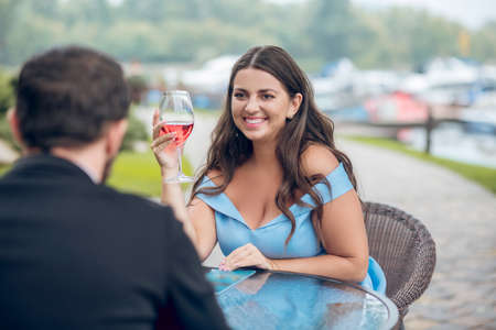 Time for two. Cheerful attentive young woman with glass looking at man sitting with back to camera