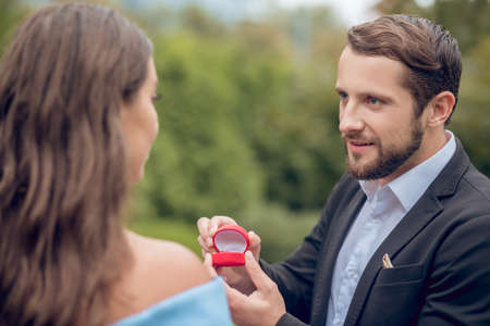 Proposal, hope. Hopeful loving young adult bearded man proposing while presenting ring in open case...
