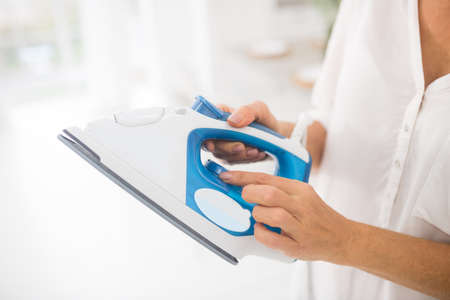 Iron, regulation. Female thin hands holding white and blue iron while turning temperature switch.の写真素材