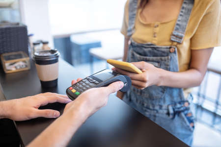 Payment, order. Female slim hands holding yellow smartphone near poster over counter in cafe