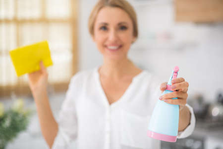 Cleaning the house. Blonde smiling woman in shirt holding a disinfecting spray in handsの写真素材