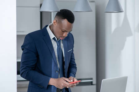 In thoughts. Elegant dark-skinned man reading something on laptop and looking thoughtful