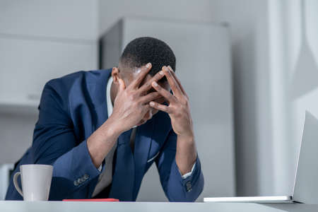 Job loss. Elegant dark-skinned man closing his head and looking frustratedの写真素材