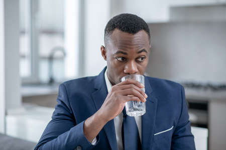 Worried. Elegant dark-skinned man looking worried and drinking waterの写真素材