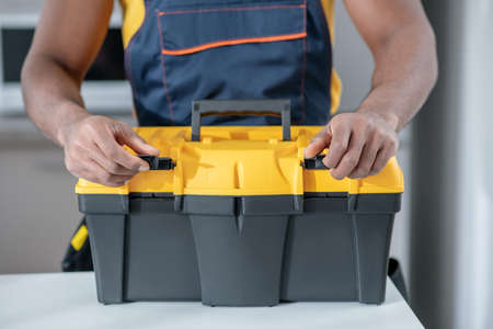 Ready to start. Dark-skinned service man standing in the kitchen and opening his tools box