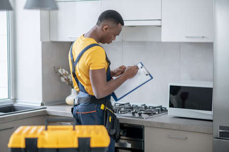 Gas stove. Dark-skinned service man standing near the gas stove in the kitchenの写真素材