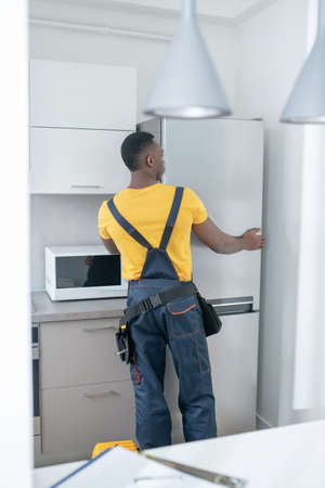 Fridge repar. Dark-skinned service man in yellow tshirt repairing the fridgeの写真素材
